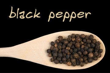 black pepper on wooden spoon isolated on black background. Latin name Piper nigrum.