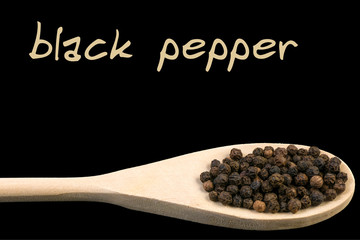 black pepper on wooden spoon isolated on black background. Latin name Piper nigrum.