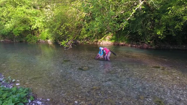 nice view fisherman and daughter with rods sit on shallow river stone father arms and kisses girl in morning 