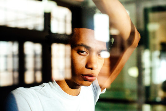 Portrait of a young man standing by the window of a large building, looking at the camera