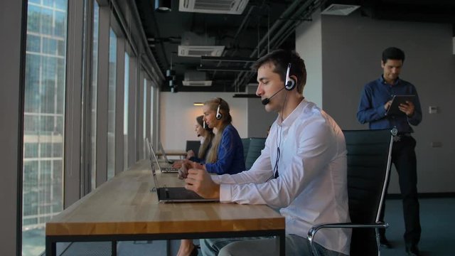 Man in shirt using a headset with laptop while working in call center office