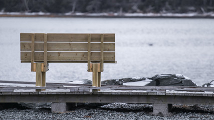 wooden bench on wooden boardwalk in winter, rocks, snow, water's edge.