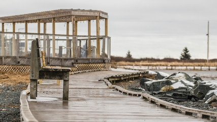 wooden bench on wooden boardwalk in winter, rocks, snow, water's edge.