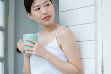 beautiful asian teen  white Tank top happiness smile enjoy freshness morning with hot drink near window with sun light