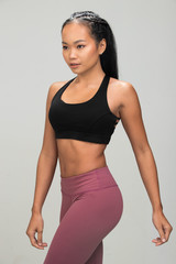 Asian Tan Skin Fitness woman exercise warm up stretch arms legs wear Black sport bra mulberry purple pants, studio lighting gray background copy space, concept Woman Can Do Sport 6 packs