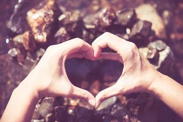 Woman hand making heart shape on the water over the rock