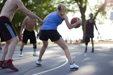 Grown woman playing basketball on outdoor court with male opponents. 