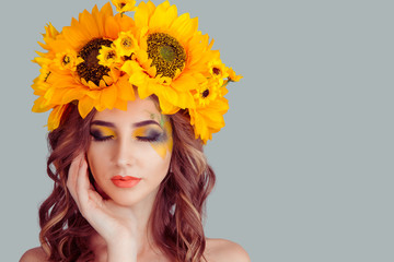 Beautiful young beautiful woman beauty model with yellow sunflowers head floral headband eyes closed looking down showing artistic makeup posing isolated on gray background. Summer style concept.