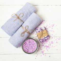 Soft clean towels bath salt a piece of natural soap laid on a light wooden background. Square frame Flat layout.