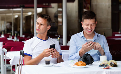 Two men sitting with coffee and looking at mobiles in cafe