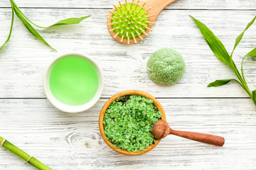 Asian spa treatment concept with natural ingredients. Spa salt, lotion, sponge near bamboo on white wooden background top view pattern