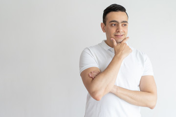 Dreamy young man touching chin and looking away