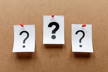 Three question marks pinned to a notice board