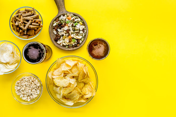 Fast food for TV watching. Snacks on desk.  Chips, nuts, rusks and beer on yellow background top view space for text