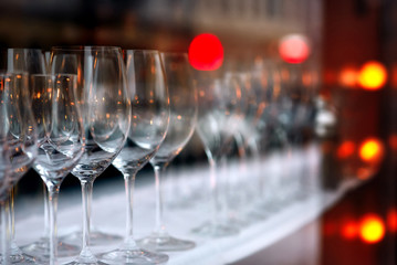 Rows of empty wine glasses with lighting showcase background in pub or night bar. Wine glasses in row on the shelf behind the window with colorful light. Interior decoration and beverage party concept
