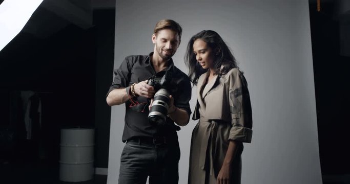 Caucasian good looking male photographer and female model watching together photos on the camera screen after photosession in the studio.