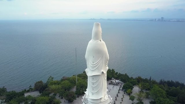 upper round motion huge white buddha statue on ocean coast against city in haze under cloudy sky in Danang