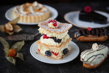 Tea and sweets on a dark background, Mille-feuille, Eclairs, Tart, Decorative with flowers, Selective focus, Closeup