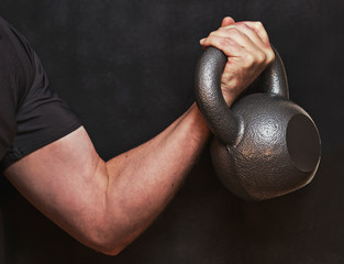 Kettlebell bicep curl, closeup of arm and hand working out with weights. Dark dramatic exercise photo for inspiration fitness over 40.