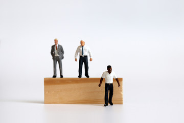 Miniature people standing on tree blocks and miniature man standing under tree blocks.