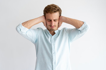 Tensed man covering ears with hands with his eyes closed