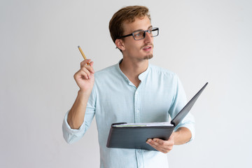 Thoughtful young man holding file, pen and having idea