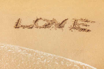 Word LOVE written in wet sand on the beach, sun shining over.