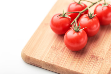 A branch of cherry tomatoes lies on a rectangular cutting board.