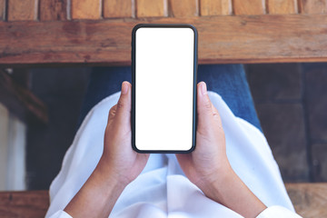 Top view mockup image of hands holding black mobile phone with blank white screen while sitting