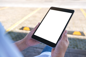 Mockup image of a woman holding black tablet pc with blank white screen while sitting in the street outdoors