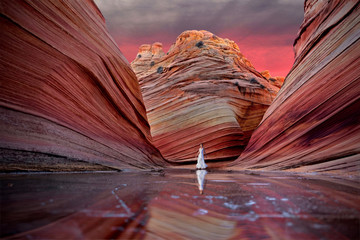 Woman standing on frozen lake with colorful rocks at sunrise.  The Wave. Vermillion Cliffs near...