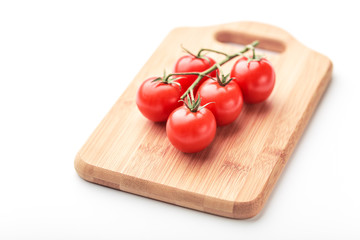 A branch of cherry tomatoes lies on a rectangular cutting board.
