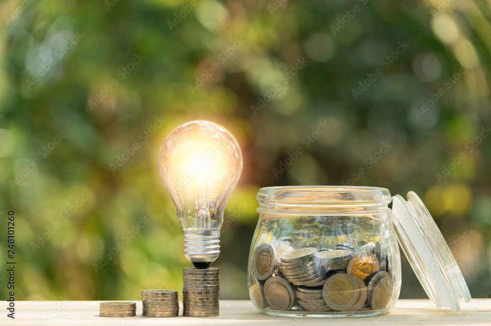 Wall mural coins and light bulb put on the table for saving money,energy concept on nature background.