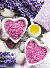 Fototapeta na wymiar Heart-shaped bowl with sea salt, oils, soap and fresh lavender flowers on a wooden background