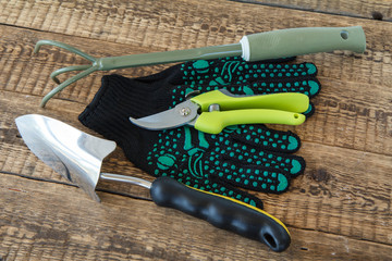 Pair of garden gloves, hand garden rake, pruner and trowel on wooden boards.