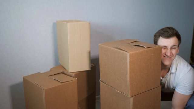 inexperienced young delivery service man takes a lot of cardboard box and boxes falling.