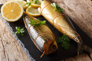 Delicious whole smoked mackerel with lemons and parsley closeup on a black slate board. horizontal