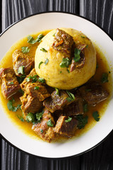 Mofongo made of plantain and chicharron served with meat and broth close-up on a plate. Vertical top view