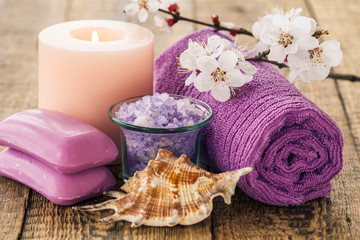 Obraz na płótnie Canvas Sea salt in glass bowl with towel, sea shell, soap for bathroom procedures and burning candle with flowering branch of apricot tree