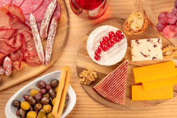 A charcuterie platter and a cheese board, shot from the top on a wooden background with pickles and wine