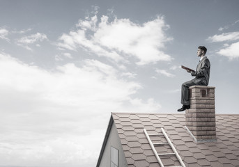 Student guy in suit on brick house roof reading book