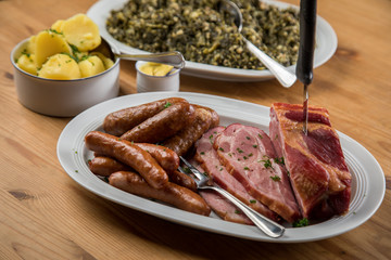 Kassler Nacken, Kohlwurst, Pinkel und Oldenburger Grünkohl auf Platten mit Kartoffeln und Senf auf Holz Tisch