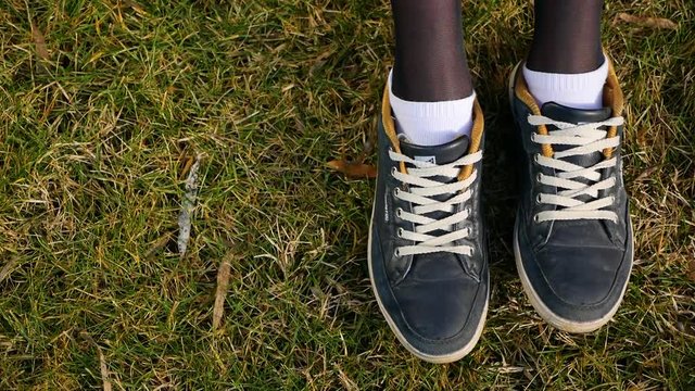 Top view, close-up female feet in white socks and sneakers moves and poses and stomps in place on green grass