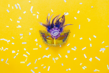 Table top view aerial image of beautiful colorful carnival season or photo booth prop Mardi Gras background.Flat lay object close up gold mask & confetti on yellow wallpaper.Space for text mock up. - obrazy, fototapety, plakaty