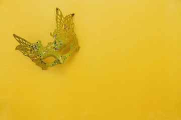 Table top view aerial image of beautiful colorful carnival season or photo booth prop Mardi Gras background.Flat lay object close up gold mask on modern yellow wallpaper.Free space for text mock up.