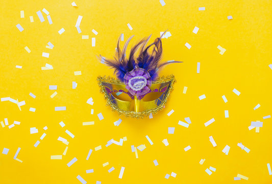 Table top view aerial image of beautiful colorful carnival season or photo booth prop Mardi Gras background.Flat lay object close up gold mask & confetti on yellow wallpaper.Space for text mock up.