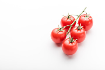 A branch of cherry tomato lies on a white surface.