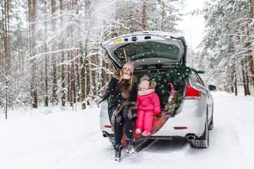 Happy mother with the little daughter and Christmas tree sitting in the car in the winter forest