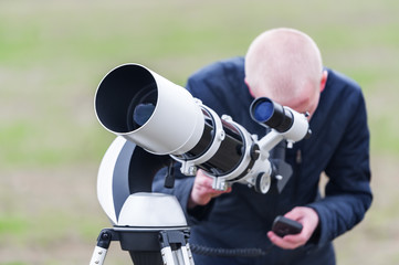 Young man looking skyward through astronomical telescope - obrazy, fototapety, plakaty