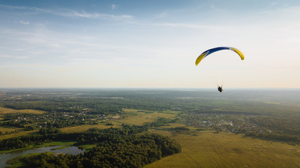 Paraglider flies over green fields. High altitude. The athlete turns the thermal current. Rise up. Weather for flights. Top view of the paraglider flying over a green field with a road. 
